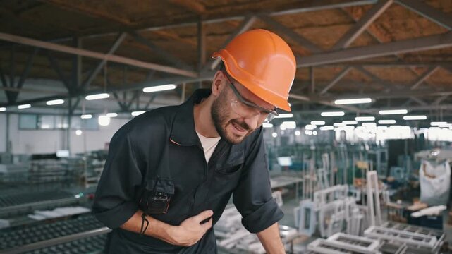 A factory worker holds his stomach and writhes in pain