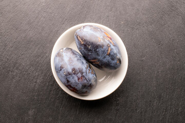 Black ripe plums with homemade kitchen utensils on slate stone, close-up, top view.
