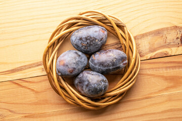 Black ripe plums with household utensils on a wooden table, close-up, top view.