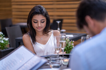 Stylish young woman reading menu during outdoor dinner with friends in summer evening