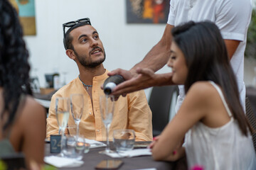 Man observing waiter pouring wine during outdoor dinner at elegant restaurant