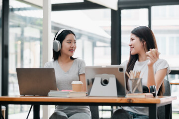 Two women working together in a bright office, using laptops and tablets, fostering creativity and collaboration.