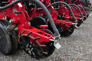  Rear part of modern pneumatic agricultural seed drill machine, red frame color, parked outside on concrete surface. 