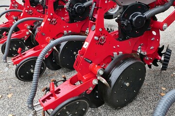 Obraz premium Detail of modern pneumatic agricultural seed drill machine, red frame color, parked outside on concrete surface. 