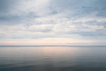Sunrise over the sea in cloudy weather. Dawn over the big lake - warm-colored sky reflects in big lake.