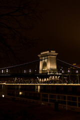 Obraz premium A captivating nighttime view of the iconic Chain Bridge in Budapest, Hungary. The bridge glows warmly under city lights, connecting the two sides of the Danube River.