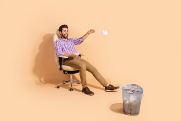 Photo of adult man employee have fun throwing paper trash into bucket sitting leather boss chair...