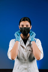 Female doctor in a black mask and blue gloves posing on a blue background.Portrait of a female doctor.Covid.Pandemic.Vaccination.Medicine concept