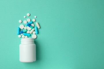 Various pills pouring out of medicine bottle on colorful background