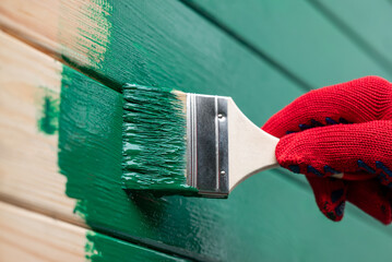 Painting outdoor house wall with a brush. Man painting wooden wall in green color, renovating...