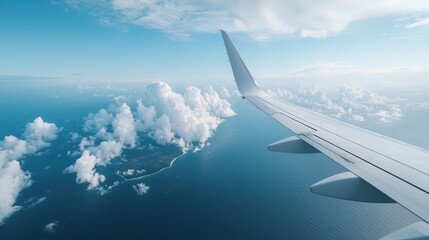 Obraz premium Aerial view from an airplane wing, showcasing clouds and a serene ocean landscape under a bright blue sky.