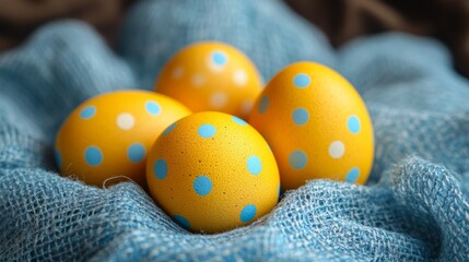 Five yellow eggs, each dotted with blue polka dots, are nestled in bluish fabric, creating a visually appealing contrast perfect for festive Easter decoration.