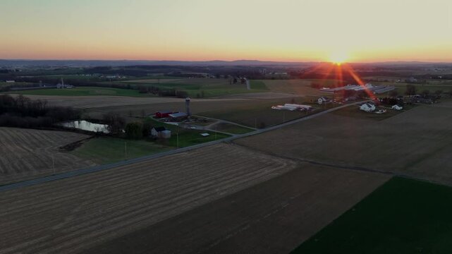 Rural landscape of USA with Road and farm houses during golden sunset. Rising drone wides shot at dusk. Beautiful weather in autumn. Agricultural fields with pattern.