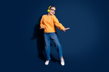 Full size photo of pretty senior female dance listen music headphones wear trendy yellow outfit isolated on dark blue color background