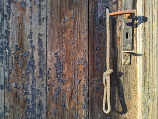 The worn wooden surface of an old door with a metal handle, lock and rope for opening. Brown textured background with space for text and logo.