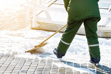 Utility worker in action shoveling snow from slippery sidewalk during sunny winter day to ensure...