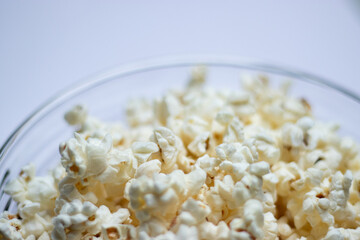 Close up of tasty popcorn in a glass bowl on white table background 
