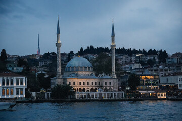 Naklejka premium Mosque rising on the Bosphorus shores, featuring illuminated minarets and dome, creates a picturesque twilight scene in Istanbul, Turkey