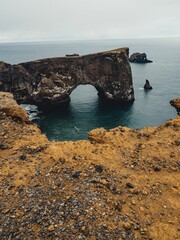 Dyrholaey Arch in Iceland with rugged coastline and overcast sky, showcasing geological formations.