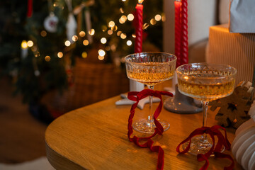 Glass glasses with champagne and red velvet ribbon near the Christmas tree. New Year. Winter holidays.