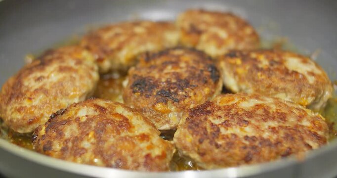 A few meat patties are fried in a frying pan in oil