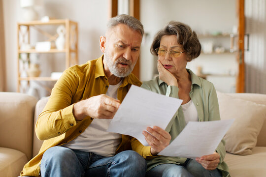 Budget planning concept. Serious senior spouses looking at papers and discussing family spends, suffering financial crisis