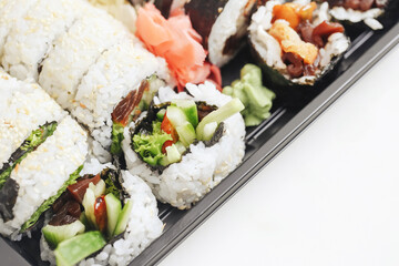 Sushi assortment in a black takeaway box. Closeup of California rolls, futomaki, and uramaki. Fresh Japanese cuisine with sesame seeds and colorful toppings. Lunch or dinner sushi to-go option.