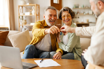 Real estate agent giving keys to excited senior couple buyers or clients, overjoyed loving spouses...