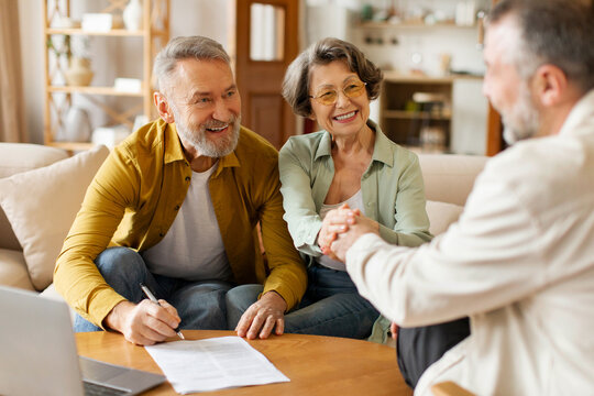 Happy senior couple of clients meeting with real estate agent, shaking hands with realtor and thanking for consultation