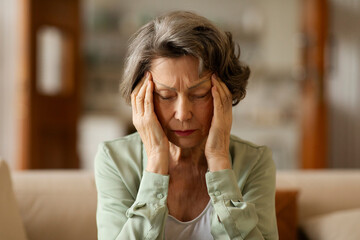 Stressed elderly woman feeling strong painful headache, touching and massaging temples with closed eyes. Migraine, high blood pressure concept