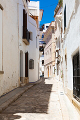 Delivery man riding a scooter in a narrow street with white houses in sitges, spain