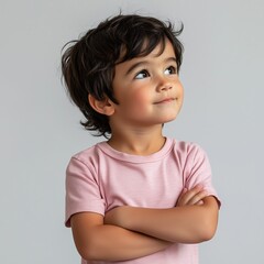 Boy  is posed with her arms crossed, standing sideways and looking up against a plain white background.
