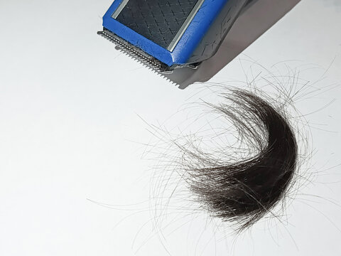 Electric hair clipper and strand of black hair lie on table. Hairdresser's services. Hair cutting technique. Trimmer for moustache, sideburns.