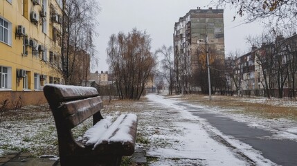 Empty park bench covered in snow beside urban apartment buildings