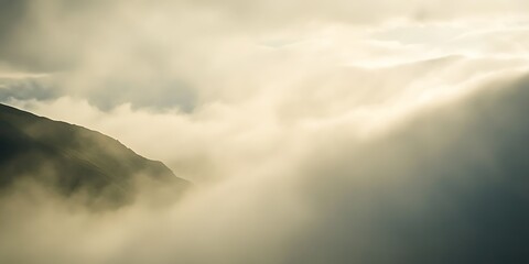 Obraz premium Misty mountain peak shrouded in fog, sunlight breaking through clouds.