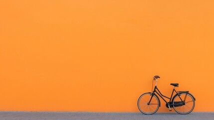 Obraz premium Against a vibrant orange wall, a black bicycle stands in a city cycling scene.