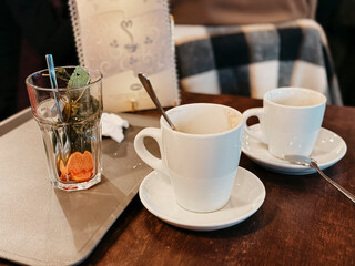 Used glass of tea with mint and citrus slice and empty coffee cups on a table, finishing eating at cafe