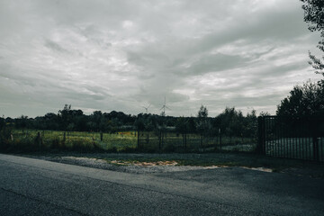 An evening park under a cloudy sky, with silhouettes of wind turbines visible in the distance
