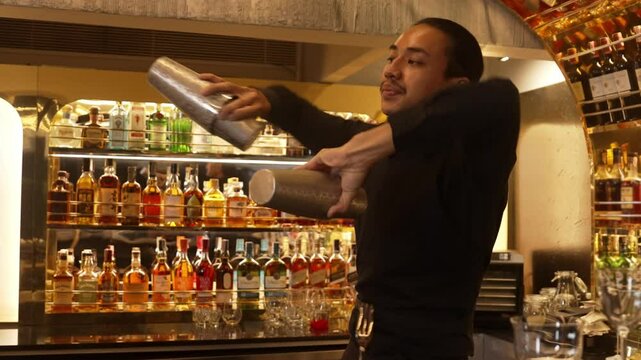 Smiling Asian smart bartender shaking with two hands in mixed cocktail in shaker preparing at luxurious counter bar, preparation special refreshment alcohol drink nightlife warm nightclub. Vinosity.