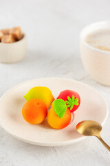 Marzipan candies in the form of fruits: pear, tangerine, lemon and strawberry in a plate with a cup of coffee on the table. Vertical orientation.