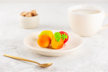 Marzipan candies in the form of fruits with a cup of coffee on the white table.