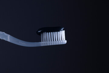 Black toothpaste on a White toothbrush with White bristles close-up on a black background