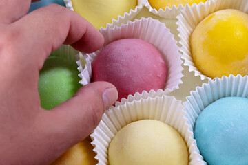 A Hand Reaches For A Vibrant Pink Mochi From An Assortment Of Colorful Mochi Desserts. The Image Captures A Moment Of Delicious Choice And Vivid Colors.