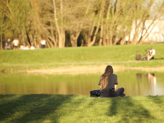 A young girl meditates on the river bank sitting on green grass. Peace of mind and emotional balance. Relaxing alone in nature. Achieving Mental Health