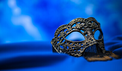 Venetian mask with gold and black beads fringe lying on a blue silk background, creating a luxurious and mysterious atmosphere