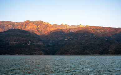 The scene captures the blue mountains above the lake during the golden hour, with calm waters mirroring the stunning landscape in Tehri Lake.