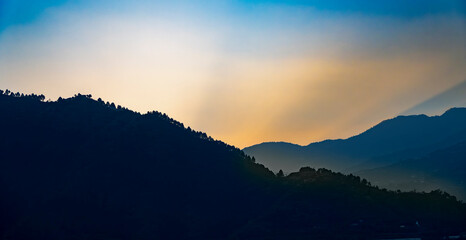 Evening blue lake waters reflect the multiple layers of mountains. Golden-yellow orange light glowing on the mountain tops adds a magical touch to the scenery of Tehri Lake.