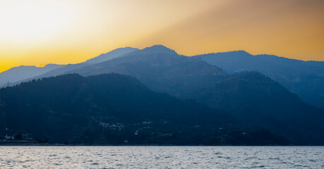 The sunset creates a dramatic scene above the blue lake, with the last rays of sunlight illuminating the mountains during the evening hours at Tehri Lake.