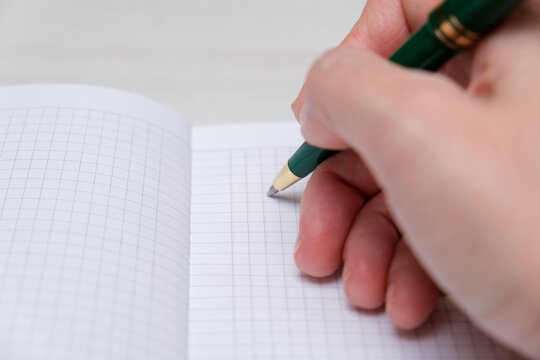 Close up of woman hand with a pen writing on notebook with laptop computer on office table. Business woman planning, making a note reminder. Student studying online, e-learning
