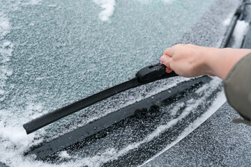 Hand trying to clean car wiper blades. Flakes of snow covered the car with a thick layer. Safe driving with working wipers and clean windshield.